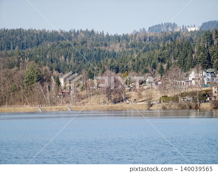 Peaceful natural scenery. Calm waters reflecting sunlight with distant cottages and rolling hills 140039565