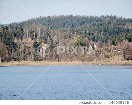 Peaceful view of forested lake scene. Serene waters bordered by forests and distant houses Peaceful view of forested lake scene. Serene waters bordered by forests and distant houses 140039566
