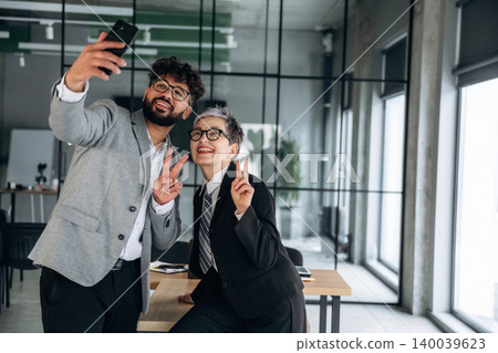Two business professionals taking a selfie in a modern office setting, showcasing a stylish interior with large windows and contemporary furniture Two business professionals taking a selfie in a modern office setting, showcasing a stylish interior with large windows and contemporary furniture 140039623