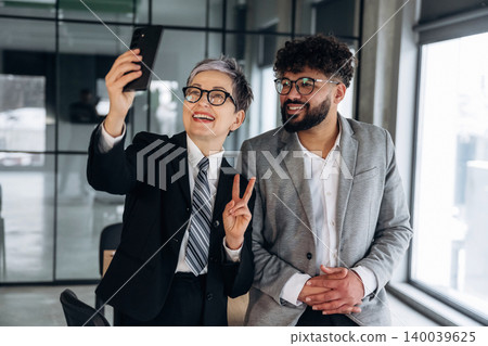 Business professionals taking a selfie together in a modern office setting, showcasing a stylish interior with large windows and contemporary furniture Business professionals taking a selfie together in a modern office setting, showcasing a stylish interior with large windows and contemporary furniture 140039625