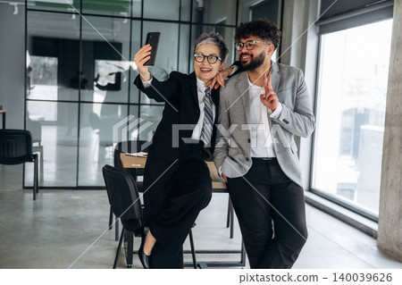Business professionals taking a selfie in a modern office setting, showcasing a stylish interior with large windows and contemporary furniture Business professionals taking a selfie in a modern office setting, showcasing a stylish interior with large windows and contemporary furniture 140039626