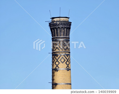 Historic brick chimney under bright sky. Weathered smokestack with ornate designs and tapering shape Historic brick chimney under bright sky. Weathered smokestack with ornate designs and tapering shape 140039909