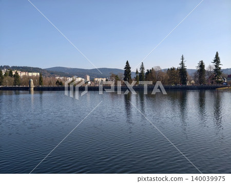 Serene landscape with water and trees. Calm lake setting surrounded by distant mountains and trees Serene landscape with water and trees. Calm lake setting surrounded by distant mountains and trees 140039975
