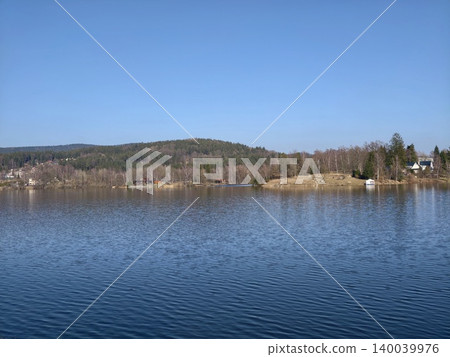 Idyllic outdoor setting showcasing serene lake bordered by hills and trees under bright sky 140039976