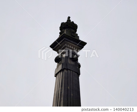 Stone obelisk against cloudy sky. Tall carved stone pillar reaching into cloudy overcast sky 140040213
