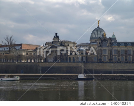 Urban waterfront with skyline view. Dometopped palace beside calm river under overcast sky with bridges 140040234