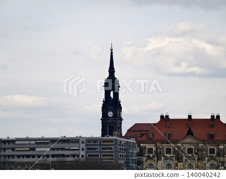 Skyscraper amid clouds. Majestic Gothic steeple rises over crowded urban environment with overcast skies Skyscraper amid clouds. Majestic Gothic steeple rises over crowded urban environment with overcast skies 140040242