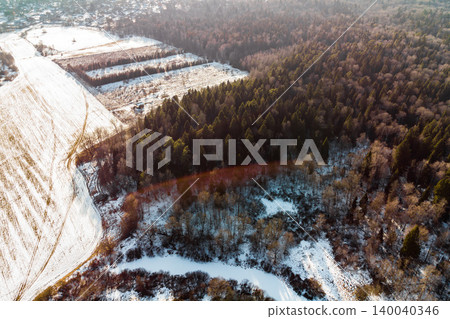 Winter aerial view of a frozen oxbow lake nestled between snowy fields and a dense forest. A serene natural landscape, sun-drenched, showcasing the quiet beauty of the season Winter aerial view of a frozen oxbow lake nestled between snowy fields and a dense forest. A serene natural landscape, sun-drenched, showcasing the quiet beauty of the season 140040346