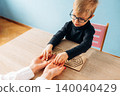 Preschool child with glasses engages in developmental activity with teacher at wooden table, colorful classroom setting with blue wall and pink chair visible in background 140040429