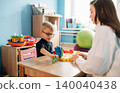 Preschool child with glasses engages in developmental play with teacher at a colorful table surrounded by educational toys in a bright classroom setting 140040438
