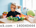 Preschool child with glasses engaged in developmental play with colorful building blocks on a wooden table in a bright classroom environment 140040444