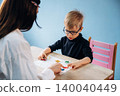 Preschool child with glasses engaged in learning activity with teacher at a wooden table, colorful educational materials visible in a bright classroom setting 140040449