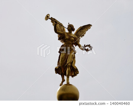 Decorative victory figure with trumpet and globe. Statue of angel celebrating triumph with symbolic motifs Decorative victory figure with trumpet and globe. Statue of angel celebrating triumph with symbolic motifs 140040460