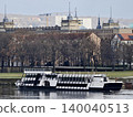 Calm river with vessel docked. Peaceful riverside view featuring classical architecture and boat mooring 140040513