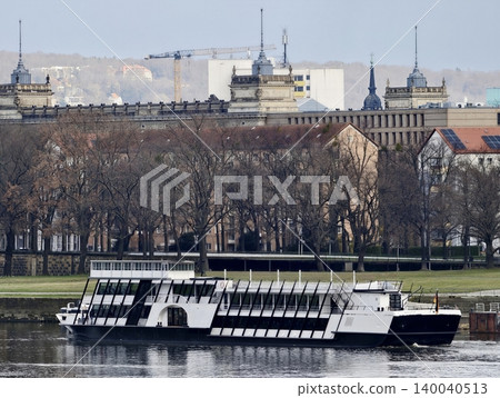 Calm river with vessel docked. Peaceful riverside view featuring classical architecture and boat mooring Calm river with vessel docked. Peaceful riverside view featuring classical architecture and boat mooring 140040513