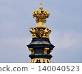 Ornamental tower with detailed crown and radiant gold accents set in historic rooftop scenery 140040523