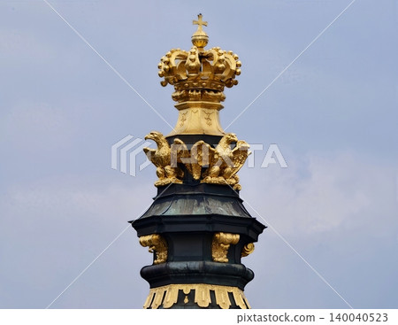 Ornamental tower with detailed crown and radiant gold accents set in historic rooftop scenery Ornamental tower with detailed crown and radiant gold accents set in historic rooftop scenery 140040523