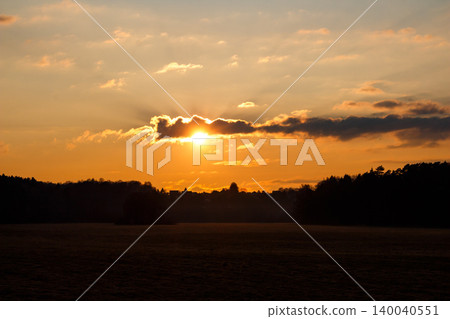 Dramatic sunset with golden rays piercing through dark clouds over a shadowy rural landscape. Breathtaking fiery sky at dusk, captivating nature Dramatic sunset with golden rays piercing through dark clouds over a shadowy rural landscape. Breathtaking fiery sky at dusk, captivating nature 140040551