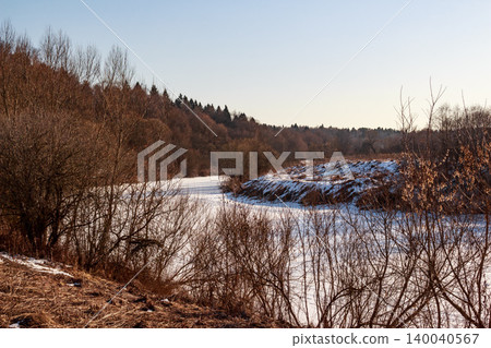 Frozen river winding through a quiet winter scene. Bare trees stand along snowy banks beneath a crisp, clear sky. Calm vibe Frozen river winding through a quiet winter scene. Bare trees stand along snowy banks beneath a crisp, clear sky. Calm vibe 140040567