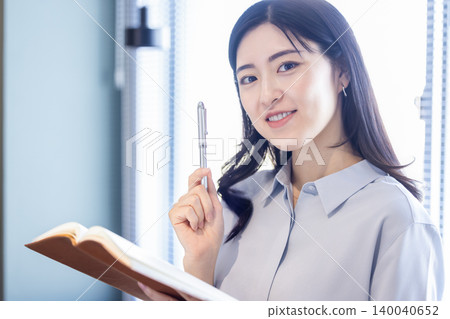 一位微笑的女士，手裡拿著筆記本和鋼筆。 140040652