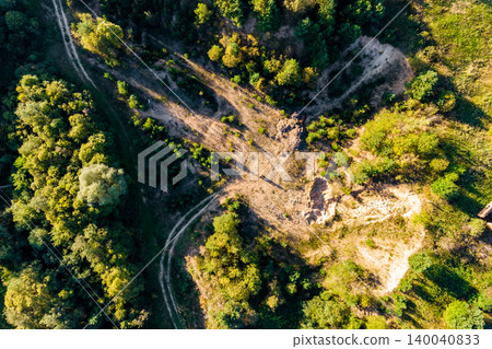 Winding dirt paths crisscross through a sun-drenched, rugged woodland with cleared areas and dense foliage. An aerial view showcasing nature and human activity Winding dirt paths crisscross through a sun-drenched, rugged woodland with cleared areas and dense foliage. An aerial view showcasing nature and human activity 140040833