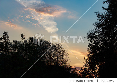 Tranquil twilight sky featuring wispy, colorful clouds streaking across soft blues and oranges, silhouetted by dark treetops. Serene evening vibe Tranquil twilight sky featuring wispy, colorful clouds streaking across soft blues and oranges, silhouetted by dark treetops. Serene evening vibe 140040869