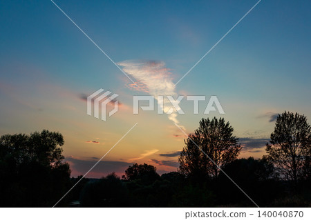 A cool funnel-like cloud, vivid and swirling, stands out in the colorful twilight sky. Dark tree silhouettes frame this unusual natural sight at dusk A cool funnel-like cloud, vivid and swirling, stands out in the colorful twilight sky. Dark tree silhouettes frame this unusual natural sight at dusk 140040870