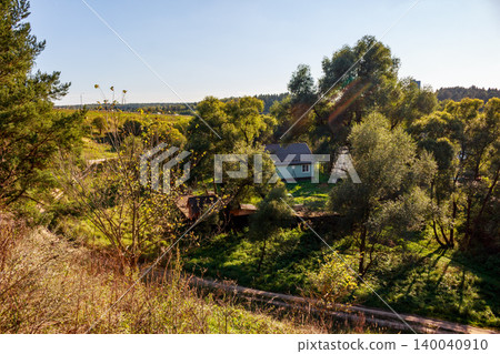A quaint little house nestled amidst lush green trees and sunlit foliage, offering a peaceful rural escape on a bright day 140040910