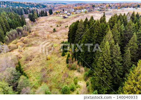 Lush evergreen forest borders a sprawling autumnal valley. Rustic village homes dot the distant hills, painting a serene, rugged natural panorama 140040933