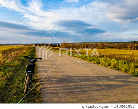 E-bike chilling roadside, golden fields under a vast sky. Perfect pause during a serene autumn ride E-bike chilling roadside, golden fields under a vast sky. Perfect pause during a serene autumn ride 140041098