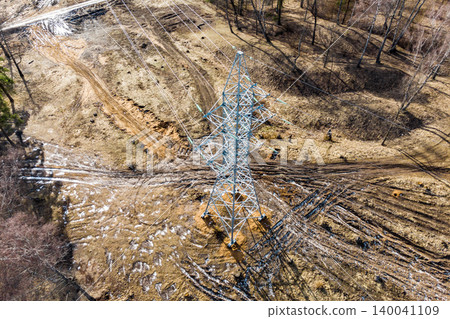Sturdy electricity pylon supports extensive power lines across a dry, disturbed landscape with sparse trees. Essential energy infrastructure in action Sturdy electricity pylon supports extensive power lines across a dry, disturbed landscape with sparse trees. Essential energy infrastructure in action 140041109