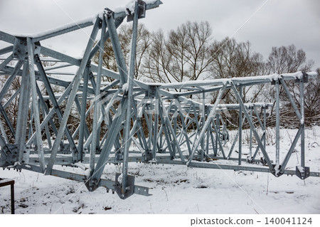 Heavy steel transmission tower sections covered in snow, resting on a wintry ground. Unassembled power pylon awaiting installation Heavy steel transmission tower sections covered in snow, resting on a wintry ground. Unassembled power pylon awaiting installation 140041124