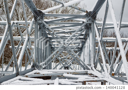 Snowy steel lattice pylon framework. Intricate metal structure, winter-coated, poised for assembly. Future power line backbone in a chilly landscape 140041128
