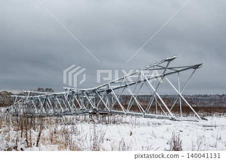 Massive power grid pylon framework rests in a snowy field, awaiting installation. Its robust metal structure, dusted with winter flakes, contrasts with the bleak sky Massive power grid pylon framework rests in a snowy field, awaiting installation. Its robust metal structure, dusted with winter flakes, contrasts with the bleak sky 140041131