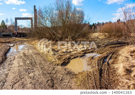 Gnarly dirt track with puddles cuts through a barren field under a bright sky, hinting at challenging travel near forgotten industrial structures Gnarly dirt track with puddles cuts through a barren field under a bright sky, hinting at challenging travel near forgotten industrial structures 140041163