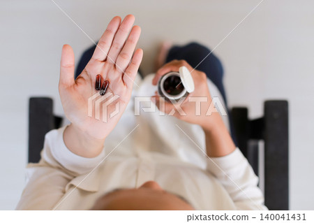 Hands hold pills and bottle against soft background. Person shows medication with calm, thoughtful gesture. Image conveys health, care, or wellness focus. Ideal for medical, lifestyle Hands hold pills and bottle against soft background. Person shows medication with calm, thoughtful gesture. Image conveys health, care, or wellness focus. Ideal for medical, lifestyle 140041431