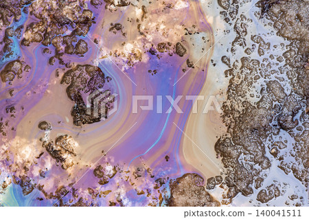 Iridescent oil spill on melting dirty snow, colorful gasoline film on a wet road surface, environmental pollution concept, chemical texture pattern in a spring puddle, toxic waste spill 140041511