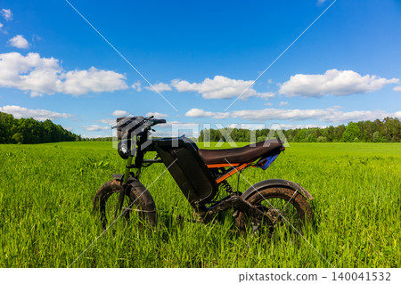 Modern electric fat bike with full suspension standing in a vibrant green meadow under a bright blue summer sky, perfect for eco-friendly off-road adventures and sustainable travel Modern electric fat bike with full suspension standing in a vibrant green meadow under a bright blue summer sky, perfect for eco-friendly off-road adventures and sustainable travel 140041532
