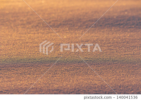 Glistening fresh snow surface textures during golden hour, illuminated by warm sunset light, soft grainy powder, sparkling winter background, crystalline frosty detail, abstract seasonal mood Glistening fresh snow surface textures during golden hour, illuminated by warm sunset light, soft grainy powder, sparkling winter background, crystalline frosty detail, abstract seasonal mood 140041536