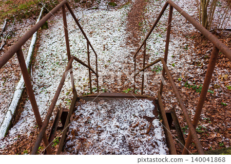 Old metal stairs leading down into a rustic forest path covered with early autumn snow and fallen dry foliage during the first frosty days of November in the woods Old metal stairs leading down into a rustic forest path covered with early autumn snow and fallen dry foliage during the first frosty days of November in the woods 140041868