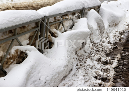 Dirty, melting snow clings to a roadside fence, revealing muddy slush and signs of a late winter thaw. A gritty, raw scene of seasonal transition 140041910