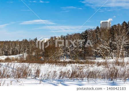 Crisp winter field scene with snow-dusted woods beneath a bright blue sky, modern buildings peek over the treeline Crisp winter field scene with snow-dusted woods beneath a bright blue sky, modern buildings peek over the treeline 140042183