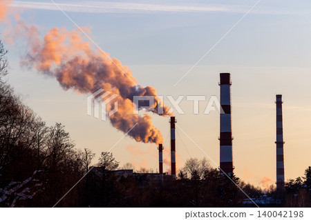 Dynamic plumes of smoke stream from industrial chimneys, painted golden by the setting sun, a stark symbol of energy and emissions Dynamic plumes of smoke stream from industrial chimneys, painted golden by the setting sun, a stark symbol of energy and emissions 140042198