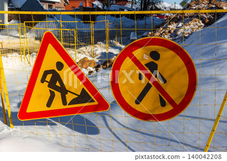 Cautionary road signs, including "Men at Work" and "No Pedestrians," are displayed on a winter construction site, fenced and covered in snow Cautionary road signs, including "Men at Work" and "No Pedestrians," are displayed on a winter construction site, fenced and covered in snow 140042208