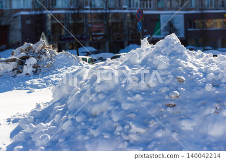 Piles of snow on city streets, cleared from roads and sidewalks, create abstract winter sculptures against a blurred urban background Piles of snow on city streets, cleared from roads and sidewalks, create abstract winter sculptures against a blurred urban background 140042214