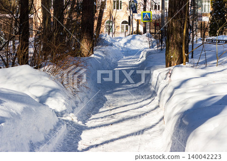 Sunny winter path, deeply carved through pristine snowdrifts, bordered by skeletal trees. A tranquil scene for peaceful seasonal walks and serene landscapes Sunny winter path, deeply carved through pristine snowdrifts, bordered by skeletal trees. A tranquil scene for peaceful seasonal walks and serene landscapes 140042223