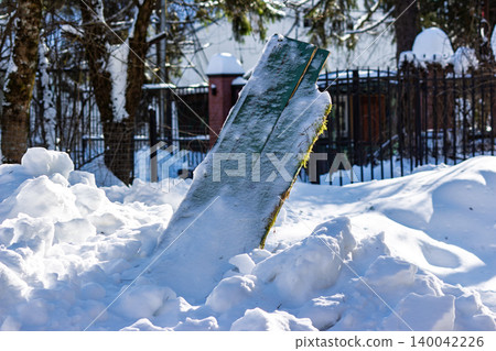 A splintered green board emerges from a thick pile of snow, likely a result of tractor snow removal. Bright winter sunlight illuminates the scene A splintered green board emerges from a thick pile of snow, likely a result of tractor snow removal. Bright winter sunlight illuminates the scene 140042226
