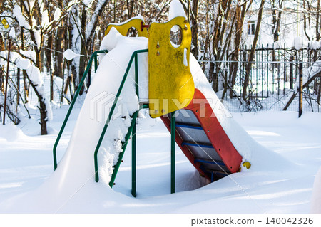 Colorful, slightly worn playground slide buried under thick, fresh white snow in a winter park setting Colorful, slightly worn playground slide buried under thick, fresh white snow in a winter park setting 140042326