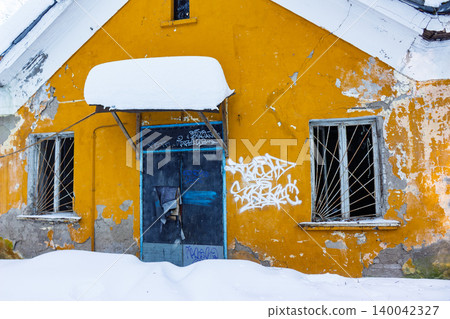 Vibrant yellow abandoned building facade with weathered walls, broken windows, graffiti, and a snow-covered entrance in winter Vibrant yellow abandoned building facade with weathered walls, broken windows, graffiti, and a snow-covered entrance in winter 140042327