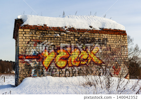 Vibrant street art adorns a weathered brick wall of an abandoned building, topped with snow. A vivid splash of color against winter's quiet decay Vibrant street art adorns a weathered brick wall of an abandoned building, topped with snow. A vivid splash of color against winter's quiet decay 140042352